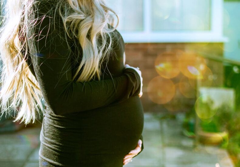 A pregnant woman enjoys a sunny day outdoors, embracing her baby bump with love.