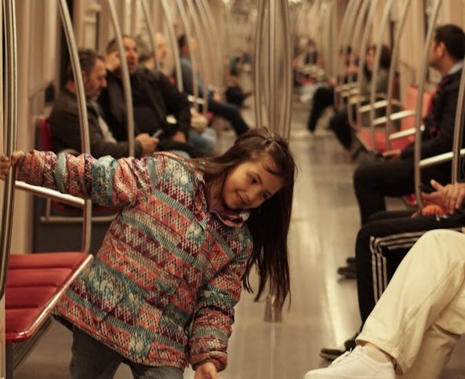A joyful child playing in a subway train, surrounded by passengers.