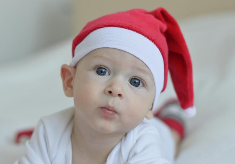 A cute baby with blue eyes wearing a red Santa hat, capturing the festive Christmas spirit indoors.