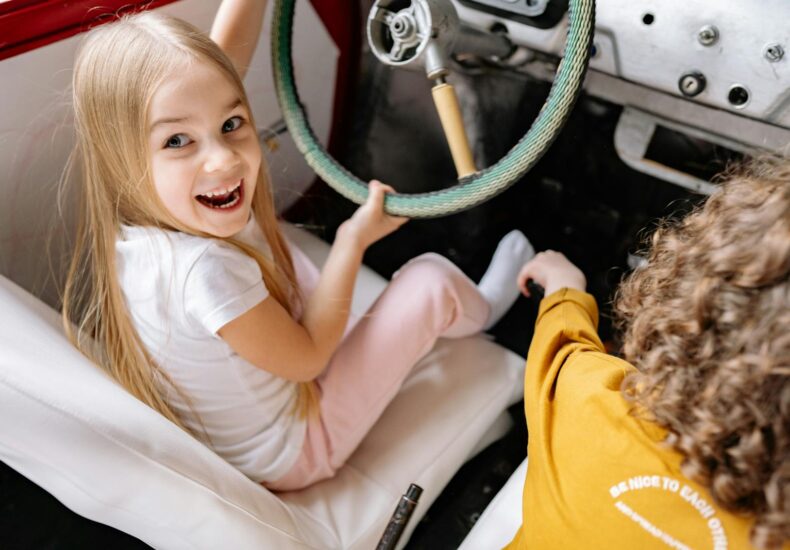 Children enjoying playtime by pretending to drive a vintage car, full of laughter and excitement.